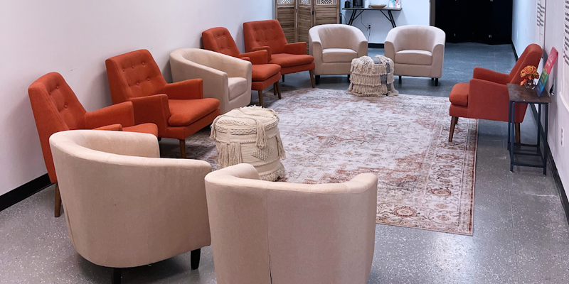 A cozy meeting room with comfortable beige and orange chairs arranged in a circle, offering a welcoming atmosphere for group discussions.