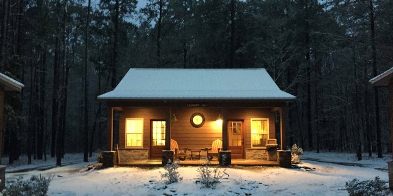  A cozy cabin warmly lit from within, surrounded by snow-covered trees at dusk, creating a peaceful and inviting winter retreat.