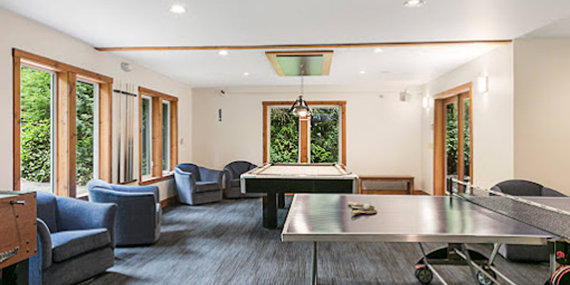 A bright recreation room with large windows, cozy chairs, and games like ping-pong and foosball, offering a comfortable and fun space for relaxation.