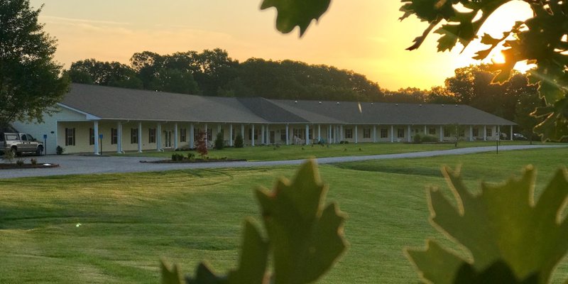 A long building sits peacefully at sunset, surrounded by lush green grass and trees, creating a serene and tranquil atmosphere.