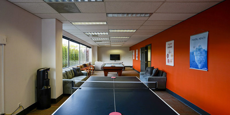 A vibrant recreational room featuring a ping-pong table, pool table, and cozy seating. Large windows provide natural light, creating an inviting space.