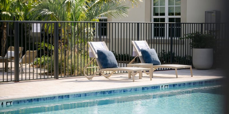 A serene poolside scene featuring two lounge chairs with blue cushions and towels, framed by tropical palm trees and a relaxing atmosphere.