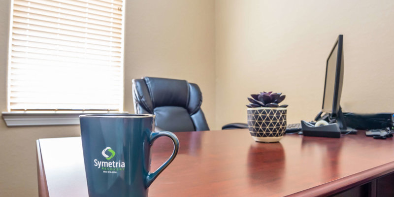 Comfortable office space with a leather chair, a wooden desk, a potted plant, and a branded mug, creating a welcoming work environment.