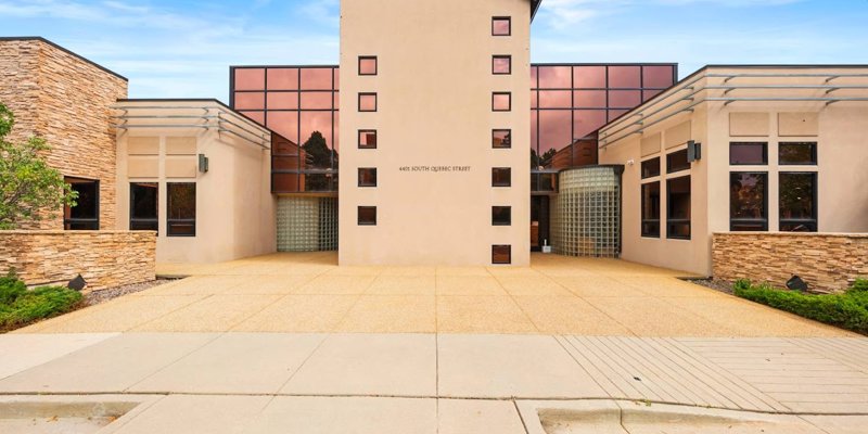 A modern building with sleek architecture and reflective glass windows, featuring stone accents and a spacious, welcoming entrance at 4401 South Quebec Street.