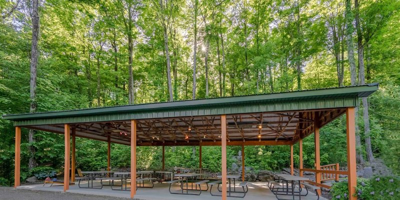 A serene outdoor pavilion surrounded by lush green trees, offering a peaceful space with picnic tables for gatherings and relaxation.