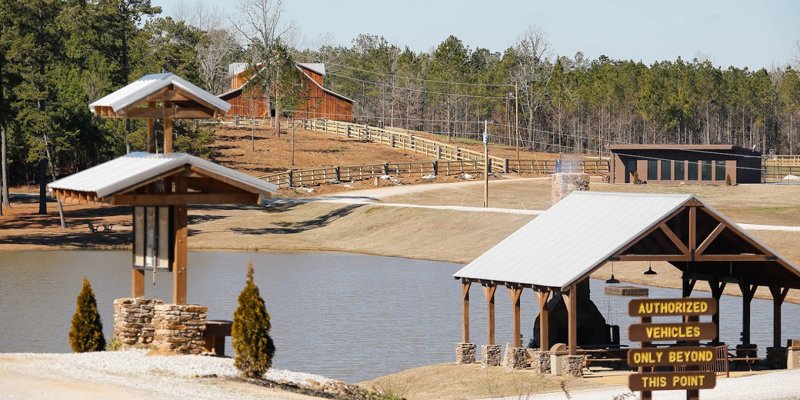  A tranquil lakeside area with wooden pavilions, rustic fences, and charming cabins surrounded by trees, creating a peaceful retreat.