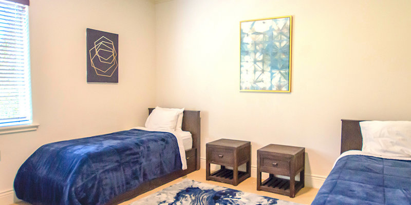 A serene bedroom with two twin beds, cozy navy blue blankets, matching nightstands, and modern artwork, creating a peaceful and stylish ambiance.