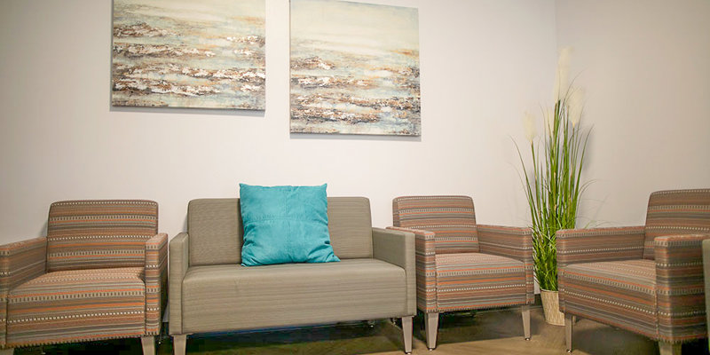  A welcoming seating area featuring comfortable striped chairs, a neutral sofa with a teal cushion, modern artwork, and a plant for decor.