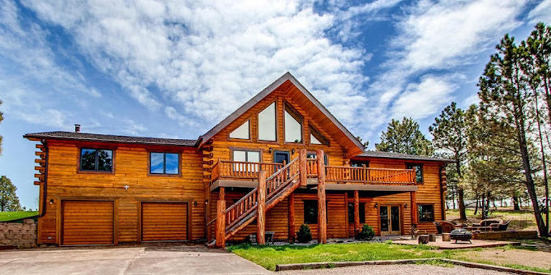 A stunning log cabin with large windows, a spacious balcony, and surrounded by tall trees, offering a rustic and welcoming retreat in nature.