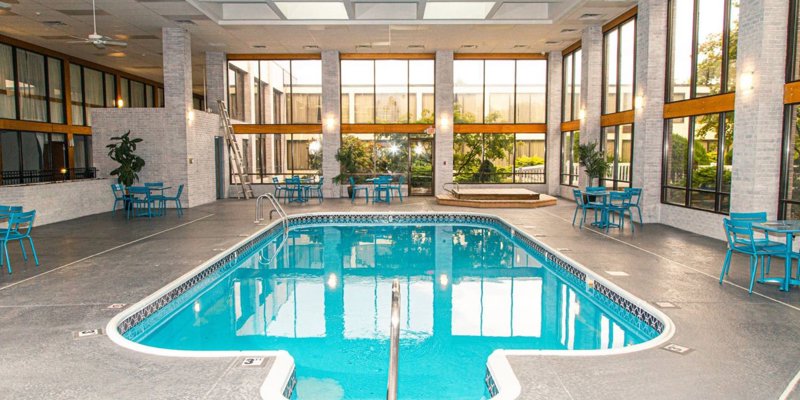 Bright indoor pool area with tall windows, modern seating, and natural light, offering a serene space for swimming and relaxation.