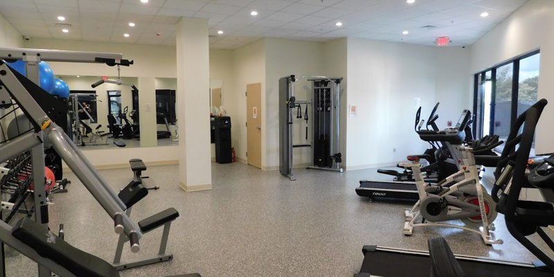 A modern fitness room equipped with treadmills, bikes, strength machines, and weights, offering a clean and spacious environment for exercise.