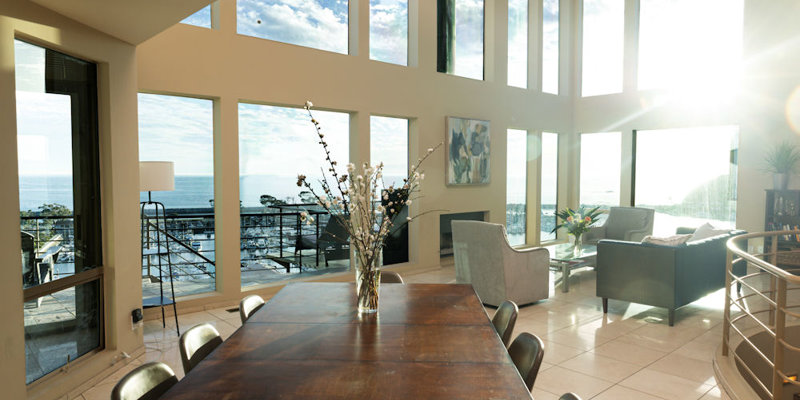 A sunlit living and dining area featuring floor-to-ceiling windows with stunning ocean views, offering a serene and inviting atmosphere.