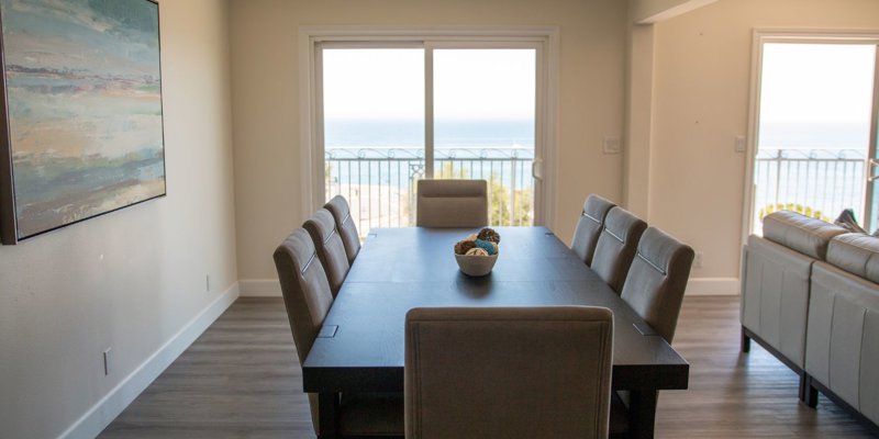 Elegant dining area with a table set for six, complemented by an ocean view through sliding doors, creating a serene, inviting space.