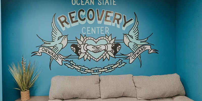 A vibrant mural at Ocean State Recovery Center featuring two doves and a heart with hands shaking, symbolizing hope and progress, above a cozy sofa.