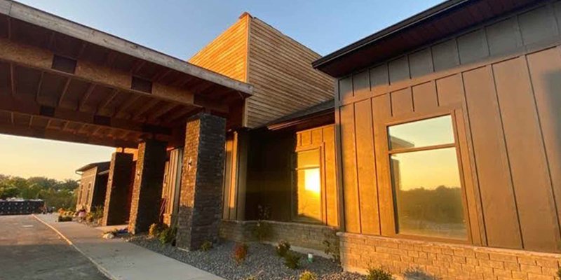 Modern recovery center building with warm, natural wood and stone elements, glowing in the soft light of a beautiful sunset, creating a serene atmosphere.