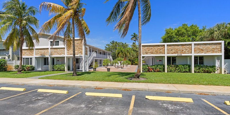 A vibrant apartment complex with palm trees and a well-maintained courtyard offers a tropical and inviting environment under a clear blue sky.