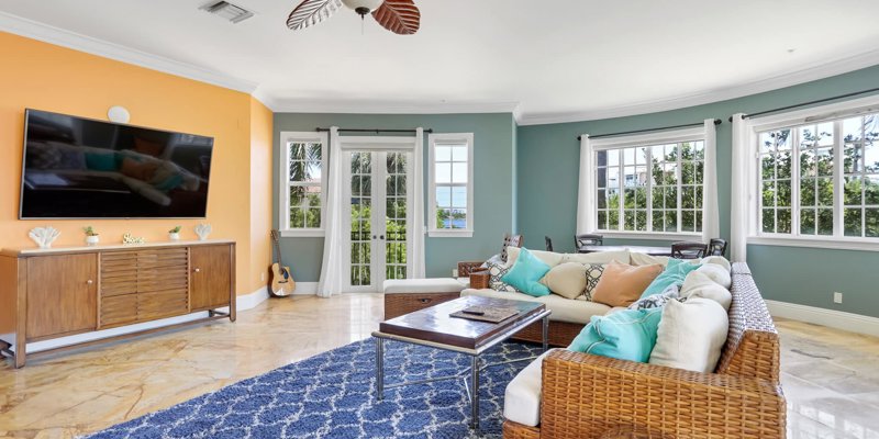 Bright and welcoming living room with large windows, vibrant wall colors, cozy wicker furniture, and a serene view of lush greenery.