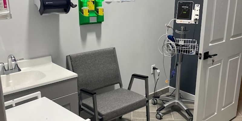  A well-equipped medical exam room with comfortable seating, an exam cart, medical tools, and a clean, modern design for patient care.