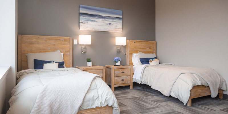 A serene shared bedroom with two cozy beds, soft lighting, wooden furniture, and calming ocean-themed artwork, creating a peaceful atmosphere.