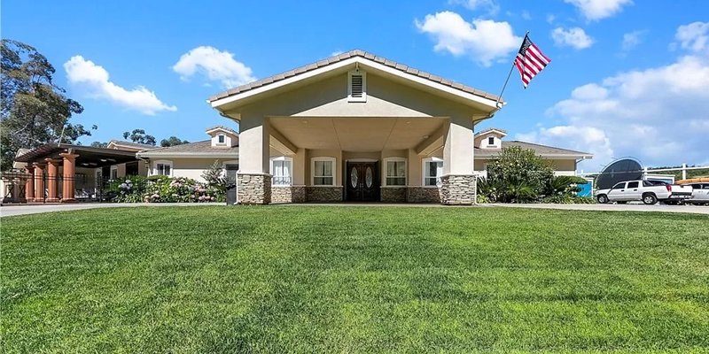  A welcoming residence with a large green lawn, elegant entrance, and an American flag proudly displayed under a bright, blue sky.