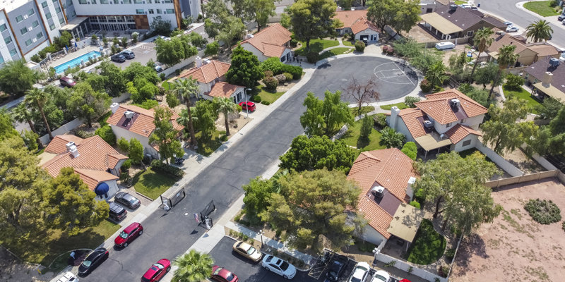 Aerial view of a peaceful residential community featuring well-maintained homes with terracotta roofs, lush greenery, and a central pool area.