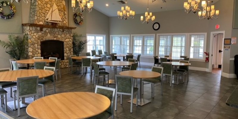 A spacious dining room with round tables, elegant chandeliers, and a cozy stone fireplace, creating a warm and inviting atmosphere.