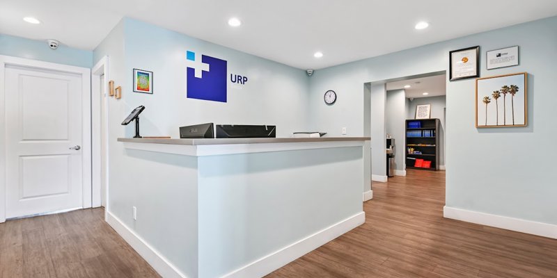 A bright and modern reception area with a clean, minimalist design, featuring light blue walls, wood flooring, and a welcoming front desk.