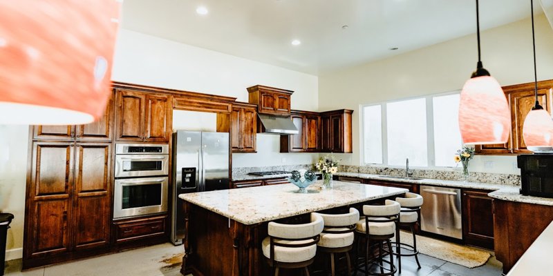  A spacious, modern kitchen with warm wooden cabinets, stainless steel appliances, and a large granite island with bar seating, ideal for gatherings.