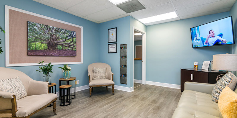 A cozy waiting room with light blue walls, comfortable seating, and calming nature artwork. Soft lighting and a TV create a relaxing atmosphere.