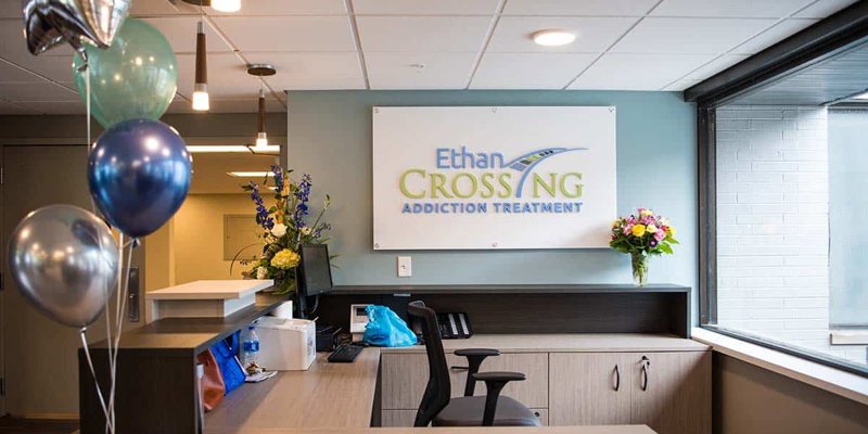  A bright and inviting reception area with a welcoming desk, colorful balloons, fresh flowers, and a sign for Ethan Crossing Addiction Treatment.