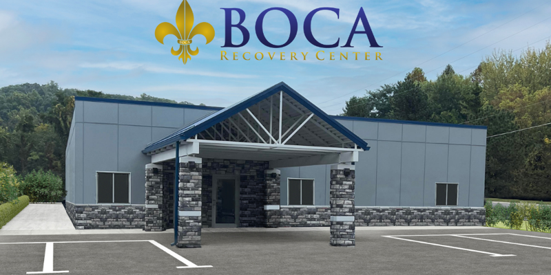 A modern recovery center building with a stone-accented entrance, ample parking, and a calm, natural backdrop, offering a welcoming environment.