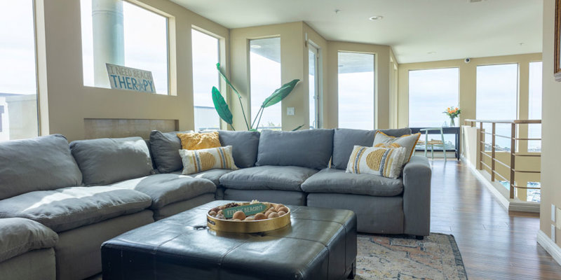  A cozy living room with a large, plush sectional sofa, bright cushions, and abundant natural light from surrounding windows offering ocean views.