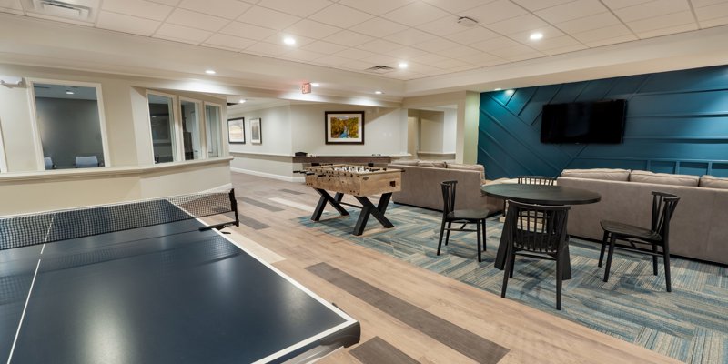 A recreational room featuring a ping pong table, foosball, and cozy seating with a TV, creating a welcoming space for relaxation and fun.