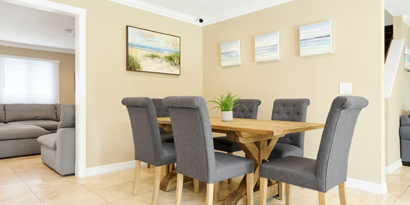  A cozy dining area with a wooden table, surrounded by gray upholstered chairs and seaside artwork, creating a warm, inviting atmosphere.