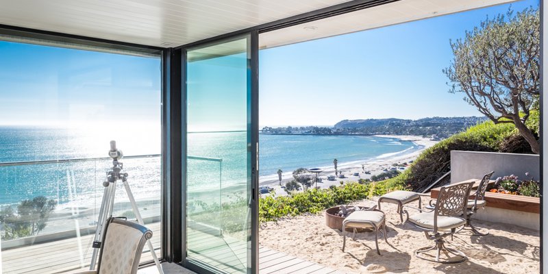 Bright oceanfront patio with sand seating area, elegant outdoor chairs, and panoramic coastal views, perfect for relaxation and serenity.