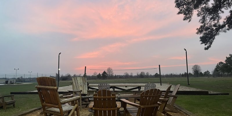 Adirondack chairs encircle a fire pit under a soft, pastel sunset, creating a serene atmosphere perfect for evening relaxation.