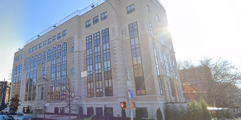 A grand, multi-story building with tall, reflective windows and intricate architectural details. The sun shines brightly, enhancing the welcoming exterior.