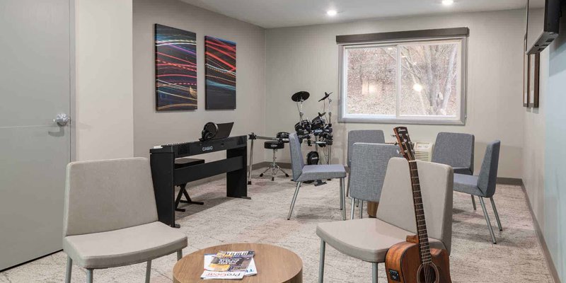 A cozy music therapy room with instruments like a guitar, keyboard, and drums, along with comfortable chairs, fostering creativity and relaxation.