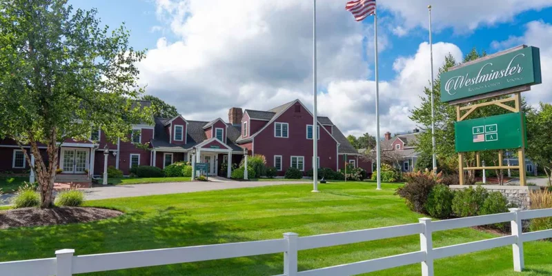 A picturesque recovery center with a classic red exterior, lush green lawns, and an American flag waving proudly, creating a welcoming environment.