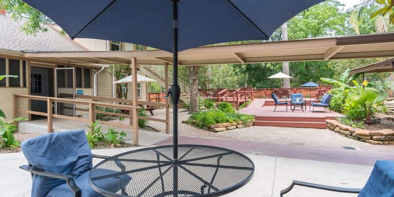 A serene outdoor patio area featuring comfortable seating under large umbrellas, surrounded by greenery and a spacious wooden deck.