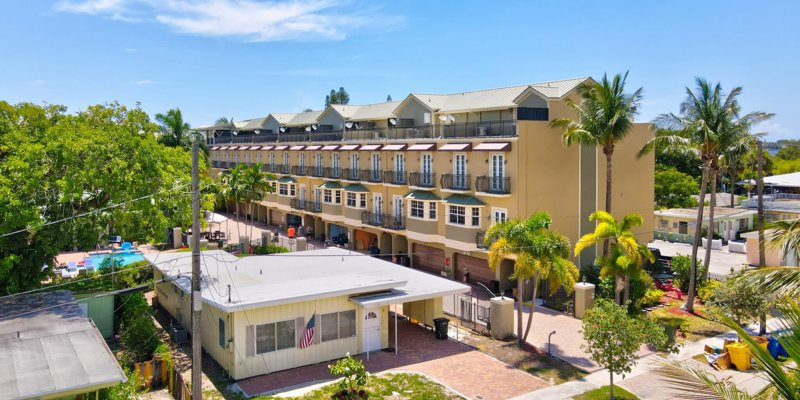  A sunny, tropical residential area with palm trees, a row of charming townhomes, and a pool. A relaxed, vibrant atmosphere.