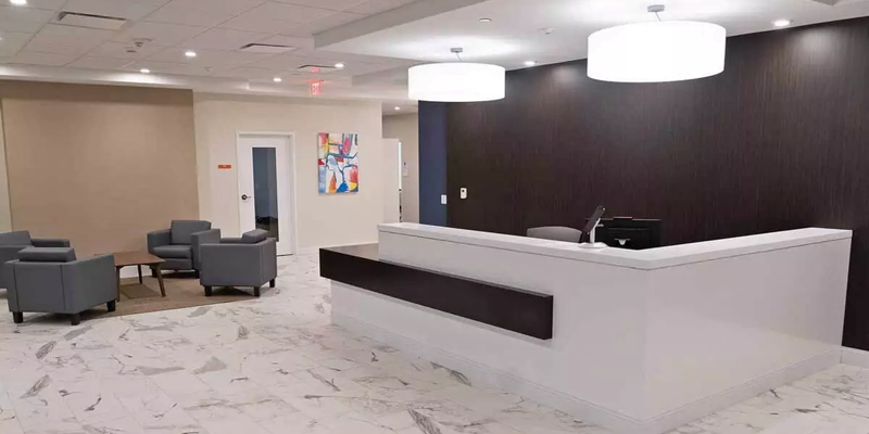 A sleek, modern reception area with marble floors, a large white desk, comfortable gray seating, and vibrant artwork on the walls.