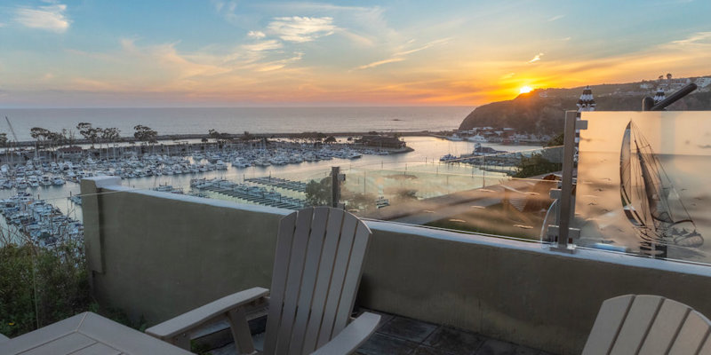  A serene sunset view over a marina, seen from a cozy outdoor seating area with Adirondack chairs, providing a perfect spot for relaxation.