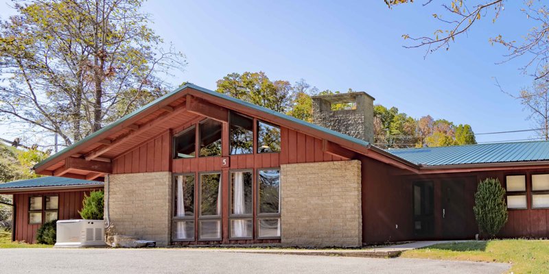 A cozy, rustic building with large windows, surrounded by trees, providing a peaceful and welcoming environment in a natural setting.