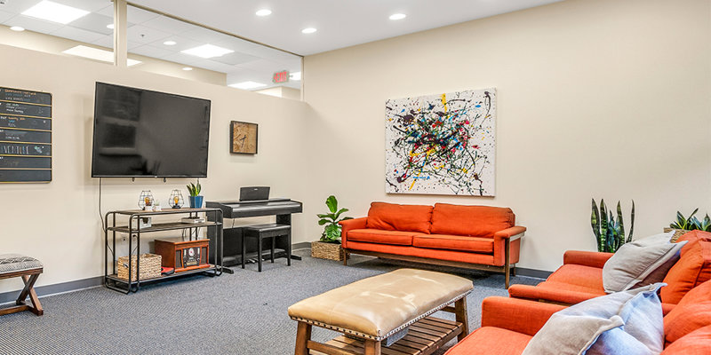 A brightly lit lounge area with vibrant orange sofas, a piano, and modern artwork, offering a welcoming and comfortable space for relaxation.