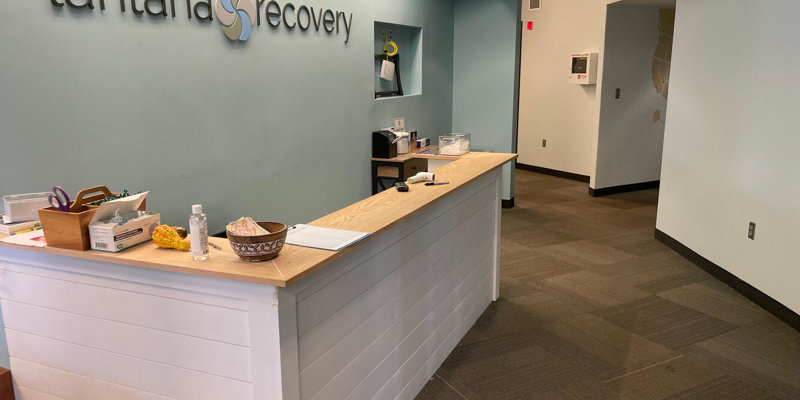  A welcoming reception area with a modern design, featuring a clean desk, calming blue walls, and the "Lantana Recovery" sign prominently displayed.