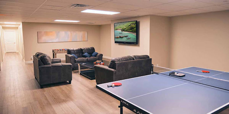 Cozy recreation room featuring a ping pong table, comfortable couches, a large wall-mounted TV, and foosball for relaxing and socializing.