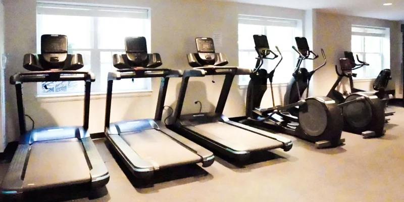 A well-equipped fitness room featuring treadmills and elliptical machines, offering a bright, inviting space for exercise and wellness.