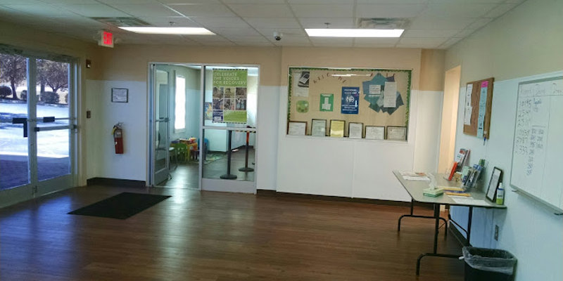 A spacious, welcoming lobby with wood floors, bulletin boards, and a table with informative materials. Bright natural light fills the space.