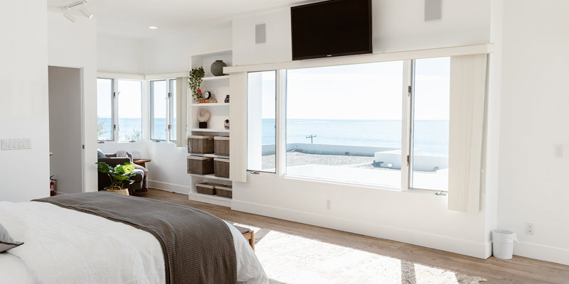  Spacious, sunlit bedroom with ocean views, cozy bed, and elegant built-in shelves, creating a serene and inviting retreat.